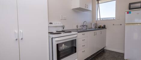 A kitchen with white cabinets, a stove, oven, sink, and a refrigerator.