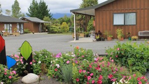 A garden area with various flowers and a wooden building with a covered patio. - Buller Bridge Motel (Westport)