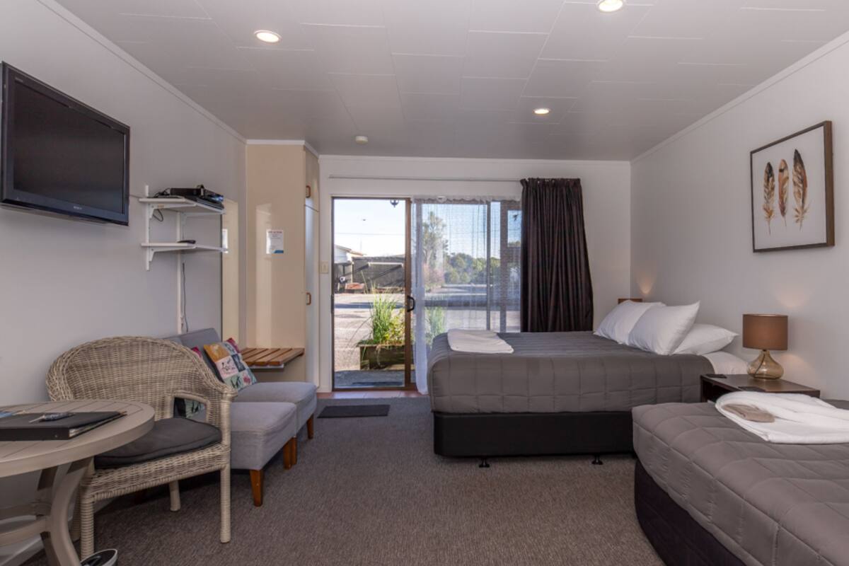 A hotel room with a bed, a sofa, a chair, a TV, and a view of the outdoors.
