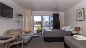 A hotel room with a bed, a sofa, a chair, a TV, and a view of the outdoors. - Buller Bridge Motel (Westport)