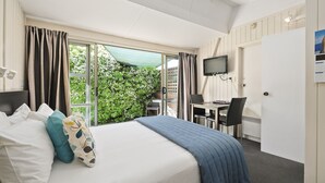 A hotel room with a bed, a desk, a chair, a TV, and a view of greenery outside. - Central Gateway Motel (Cromwell)
