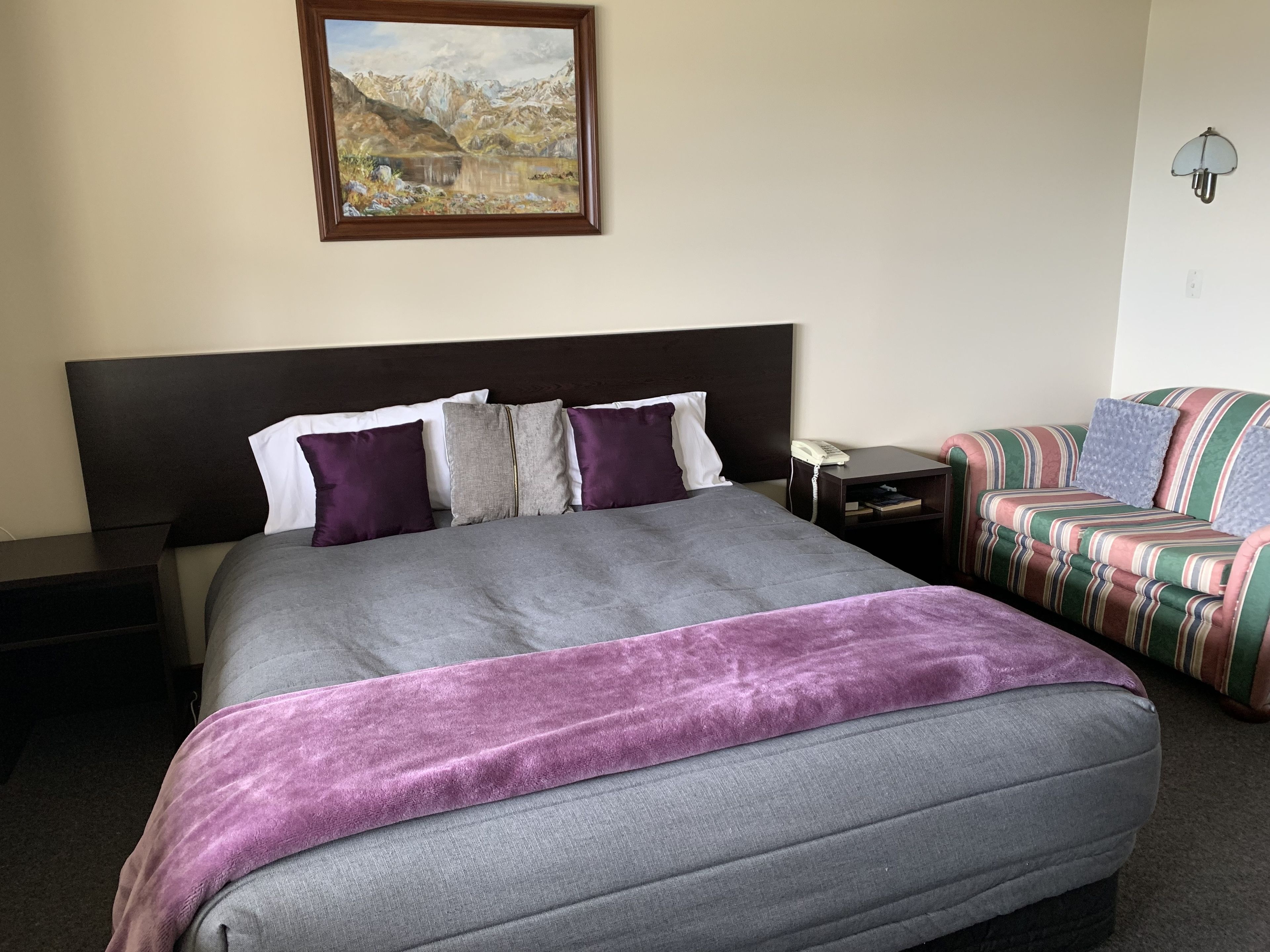 Een netjes ingerichte hotelkamer met een groot bed, een klein nachtkastje met een telefoon, een sofa en een schilderij aan de muur.