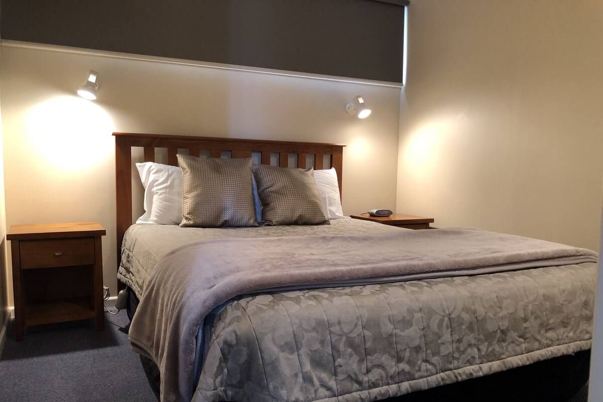 A neatly made bed with a grey floral duvet, wooden headboard, and two bedside tables with lamps.