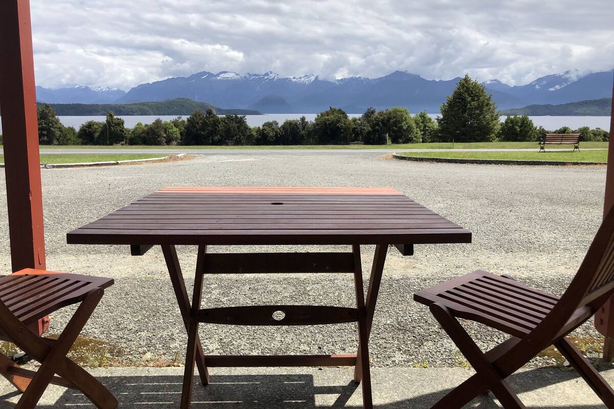 A table and two chairs in a covered outdoor area with a view of mountains and a lake.