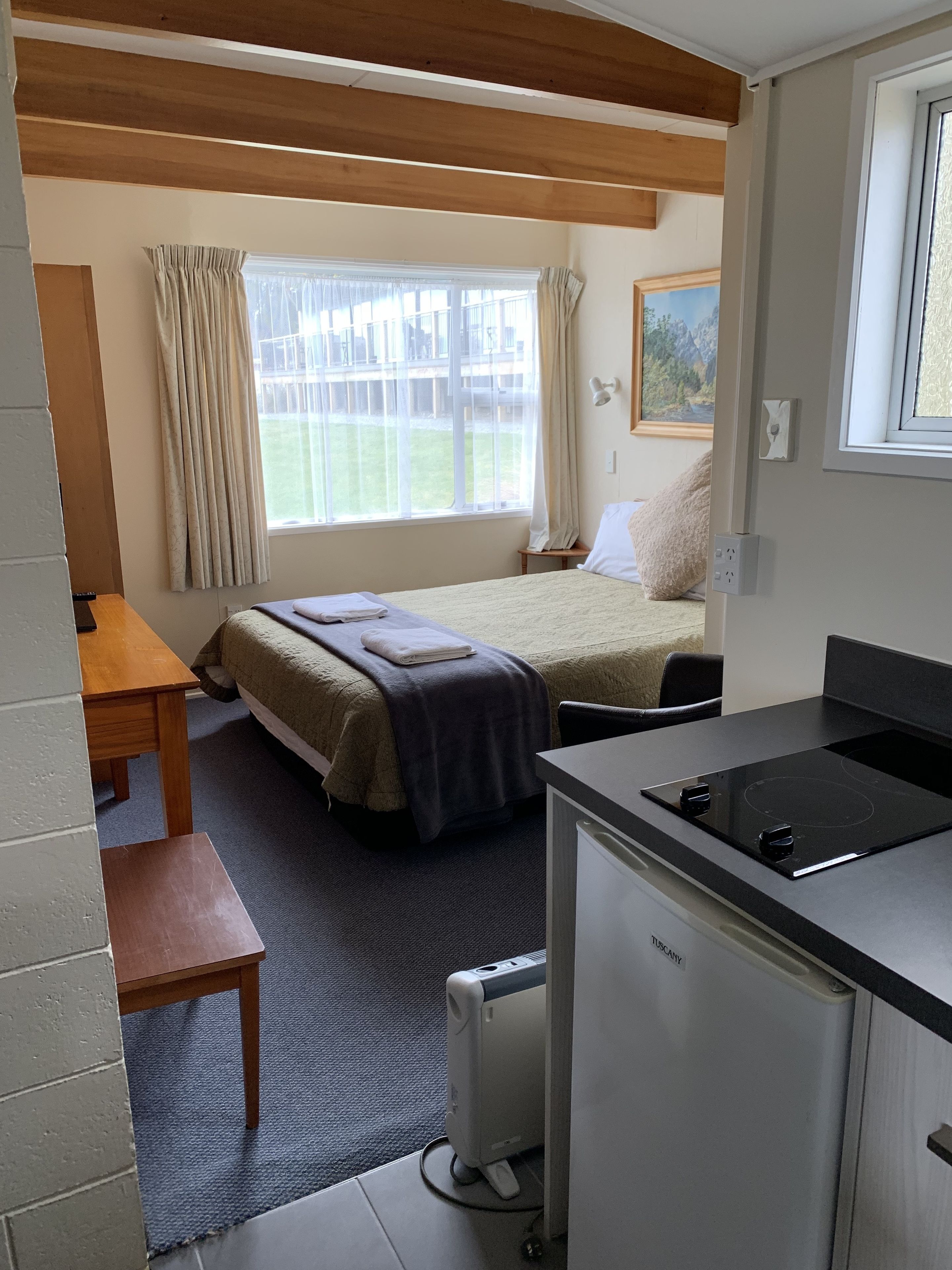 A compact room with a bed, a small desk, a kitchenette, and a window with curtains.