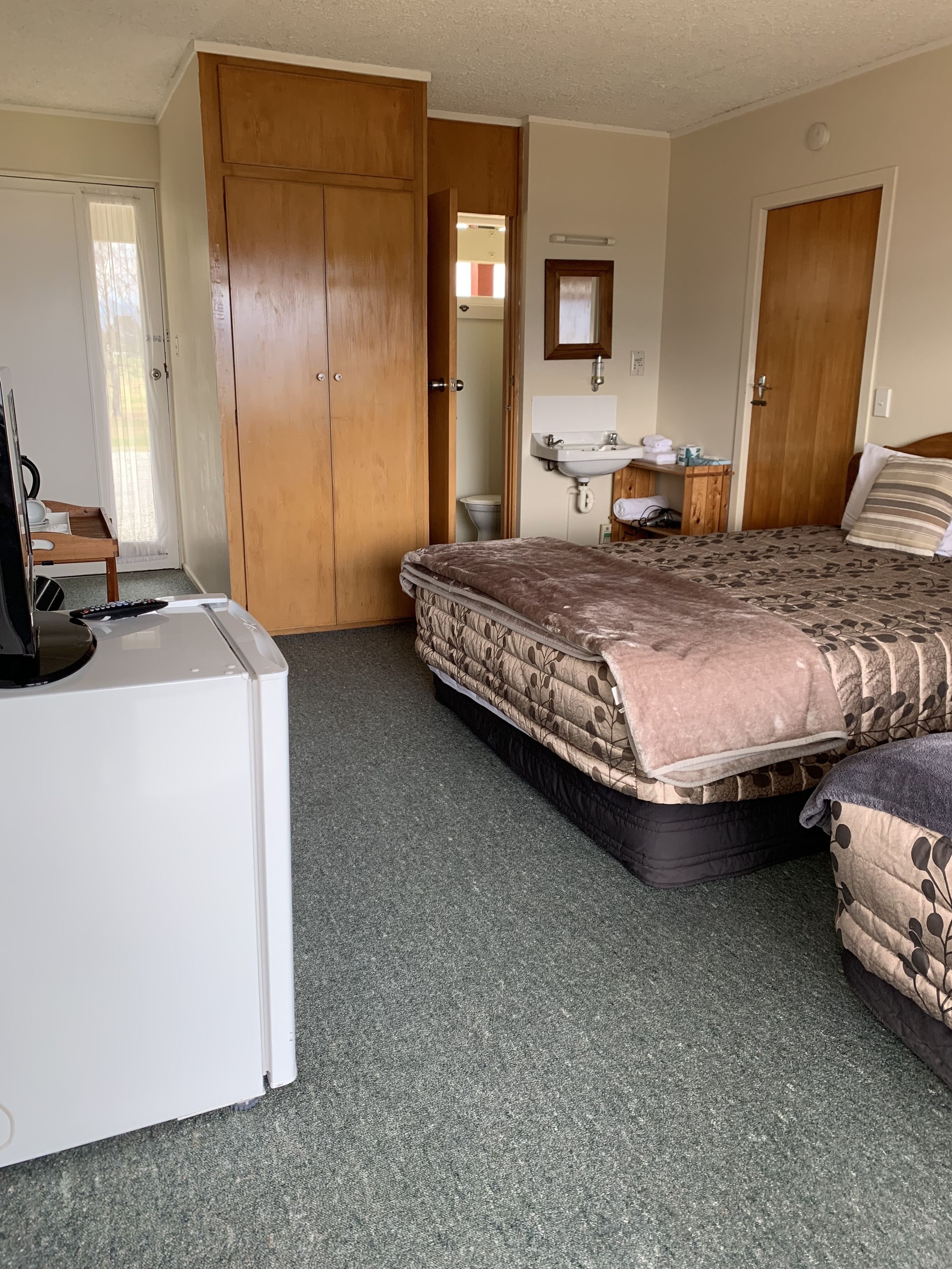 A bedroom with a bed, a desk, a wardrobe, a bathroom, and a door leading to a balcony.