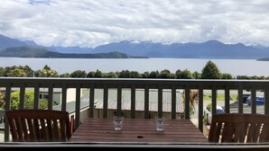 A wooden table with two glasses on a balcony overlooking a lake and mountains. - Te Anau Manapouri Lake Hotel (Manapouri)