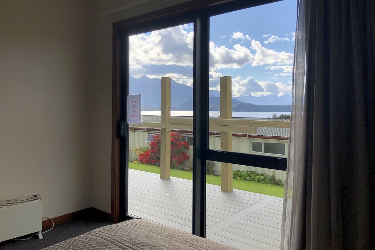 A room with a large sliding glass door leading to a balcony with a view of mountains and a body of water.