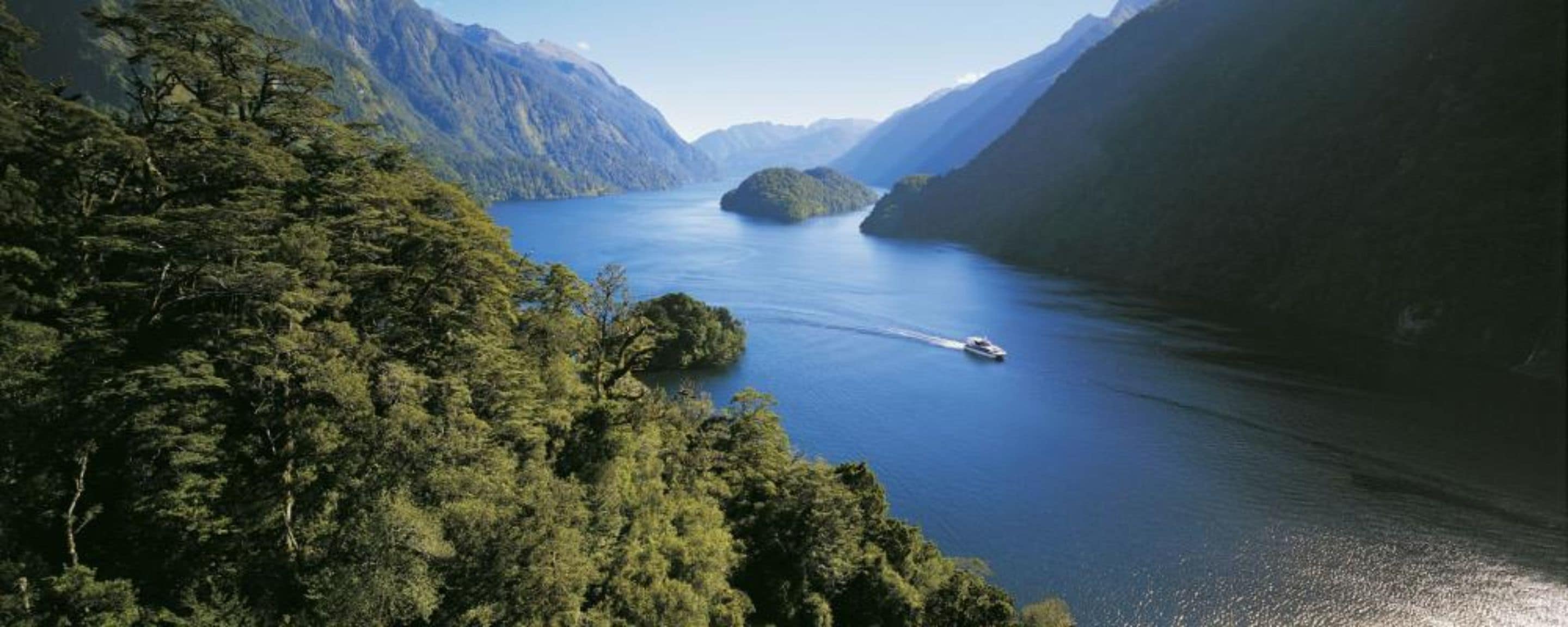 A boat on a calm lake surrounded by dense forest and mountains.