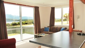 A room with a large sliding glass door leading to a balcony, a sofa, a small table, and a red chair. - Te Anau Manapouri Lake Hotel (Manapouri)