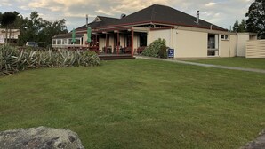 A building with a covered patio area, a sign indicating a bar and cafe, and a well-maintained lawn. - Te Anau Manapouri Lake Hotel (Manapouri)