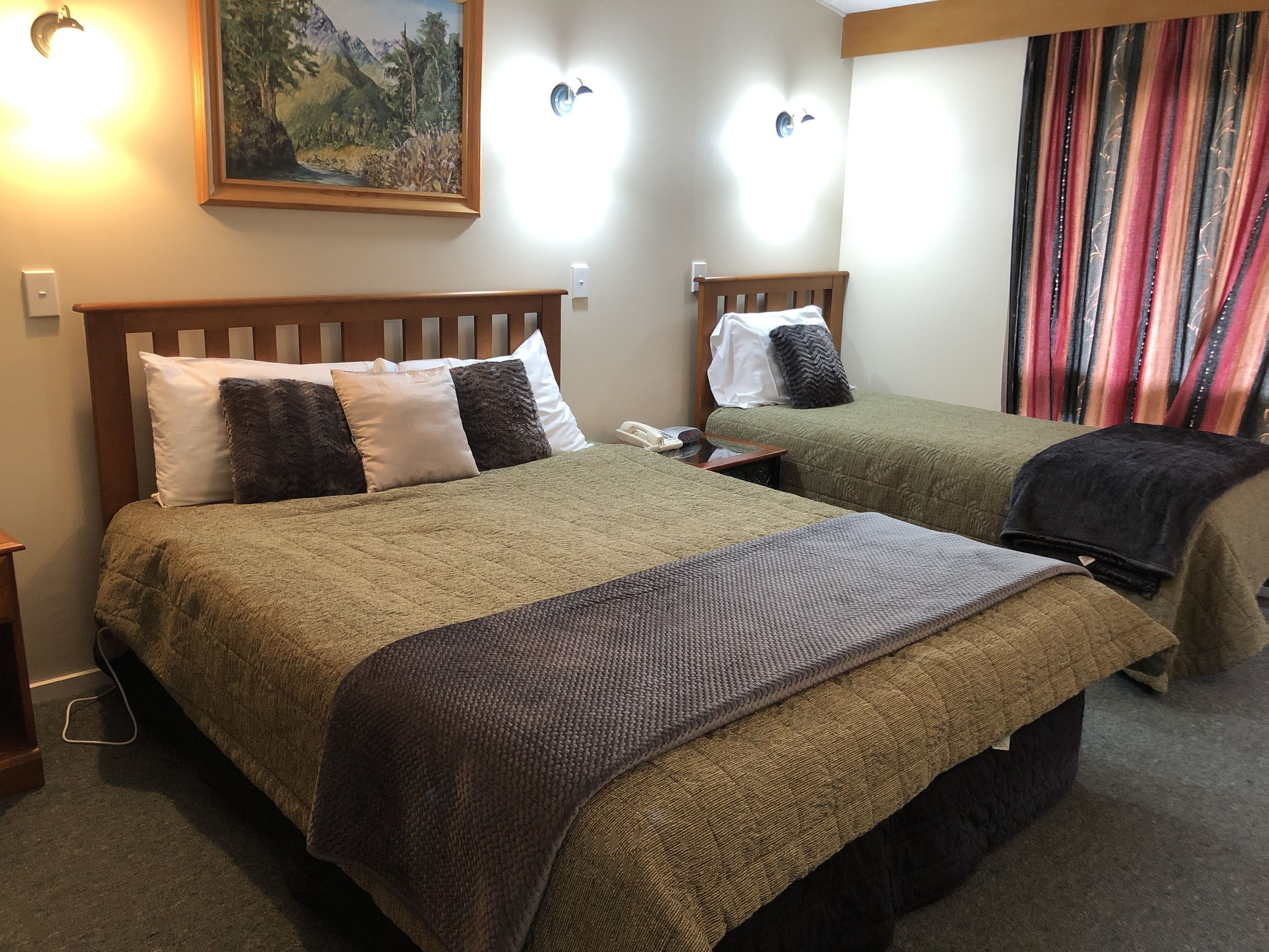 A hotel room with two beds, a painting on the wall, and a window with curtains.