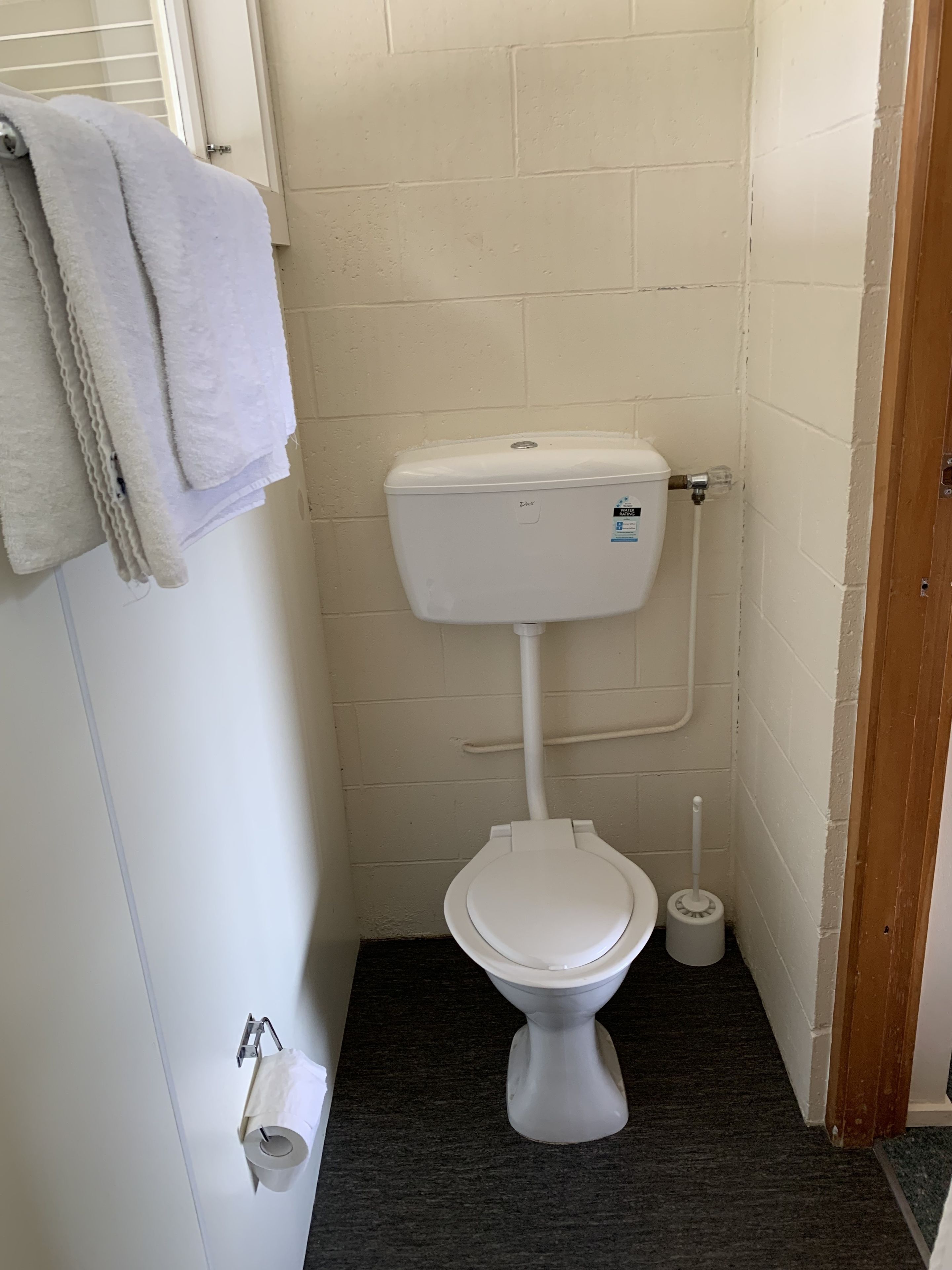 Une petite salle de bain propre, équipée de toilettes, d’un porte-serviettes et d’un support à papier toilette.