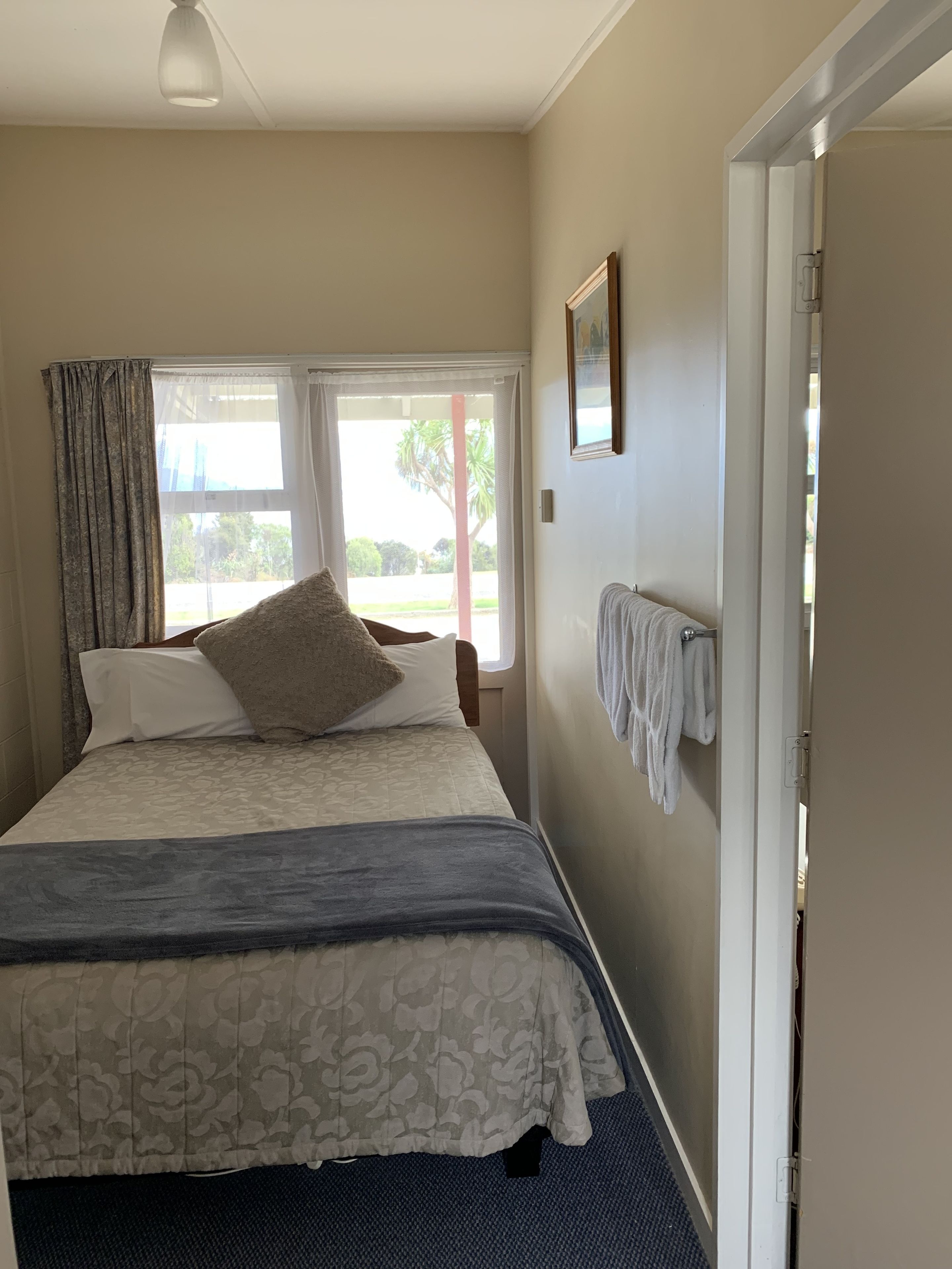 Un dormitorio con cama, ventana, puerta y un perchero para toallas.