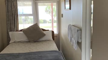 Un dormitorio con cama, ventana, puerta y un perchero para toallas.