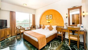 Una habitación de hotel con una cama grande, un escritorio con espejo, televisión y vistas al exterior.