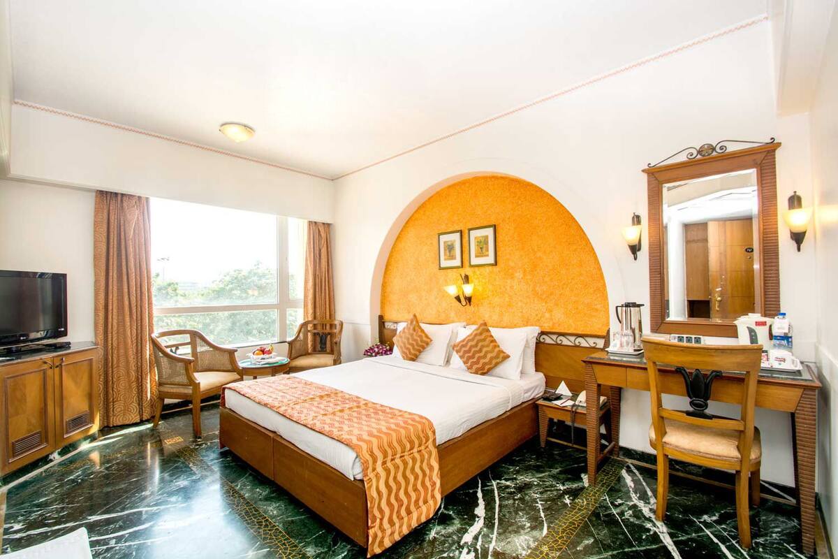 A hotel room with a large bed, a desk with a mirror, a television, and a view of the outdoors.
