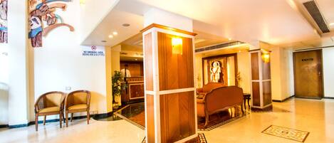 A lobby with a reception desk, two wooden chairs, a wooden pillar, and a sign indicating a no smoking area.