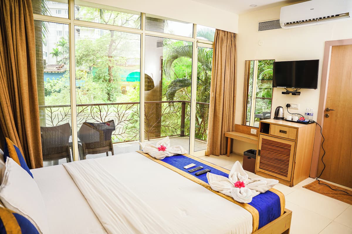Habitación de hotel con una cama grande, un escritorio con televisor y un balcón con vistas a zonas verdes.