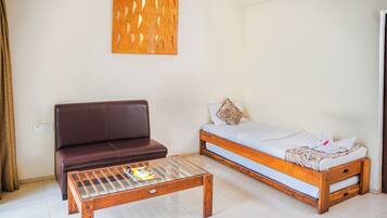 A room with a brown leather sofa, a wooden bed with white bedding, and a glass-top coffee table with magazines.