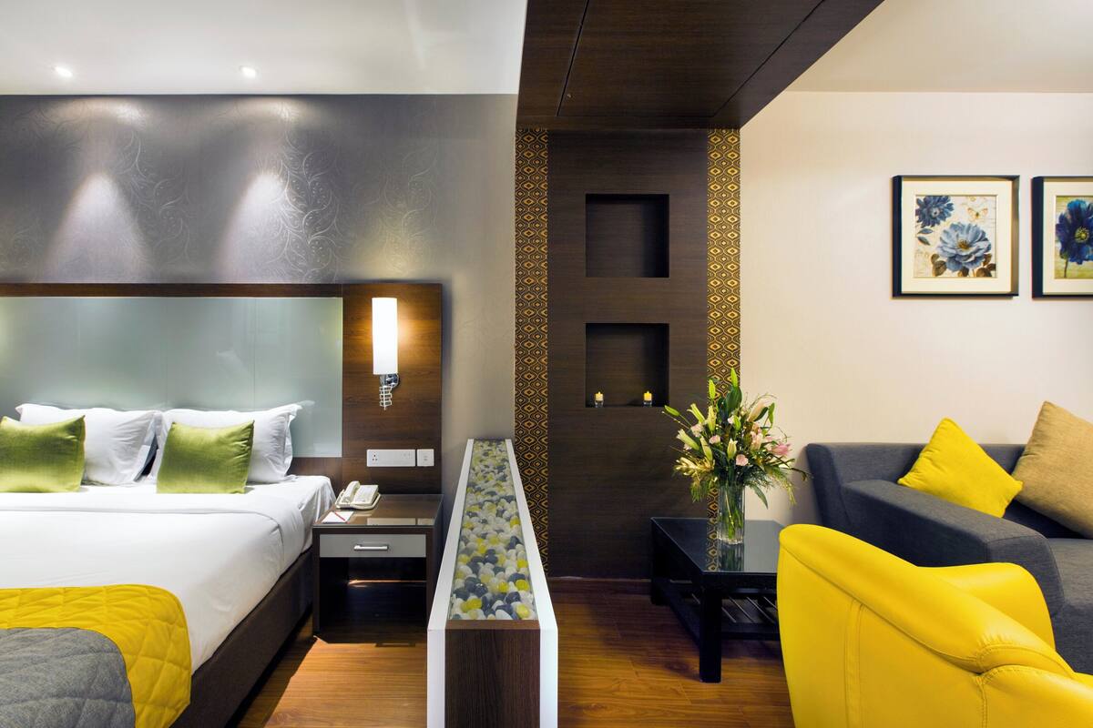 A modern hotel room with a large bed, a bedside table, a desk, a sofa, and a decorative vase.