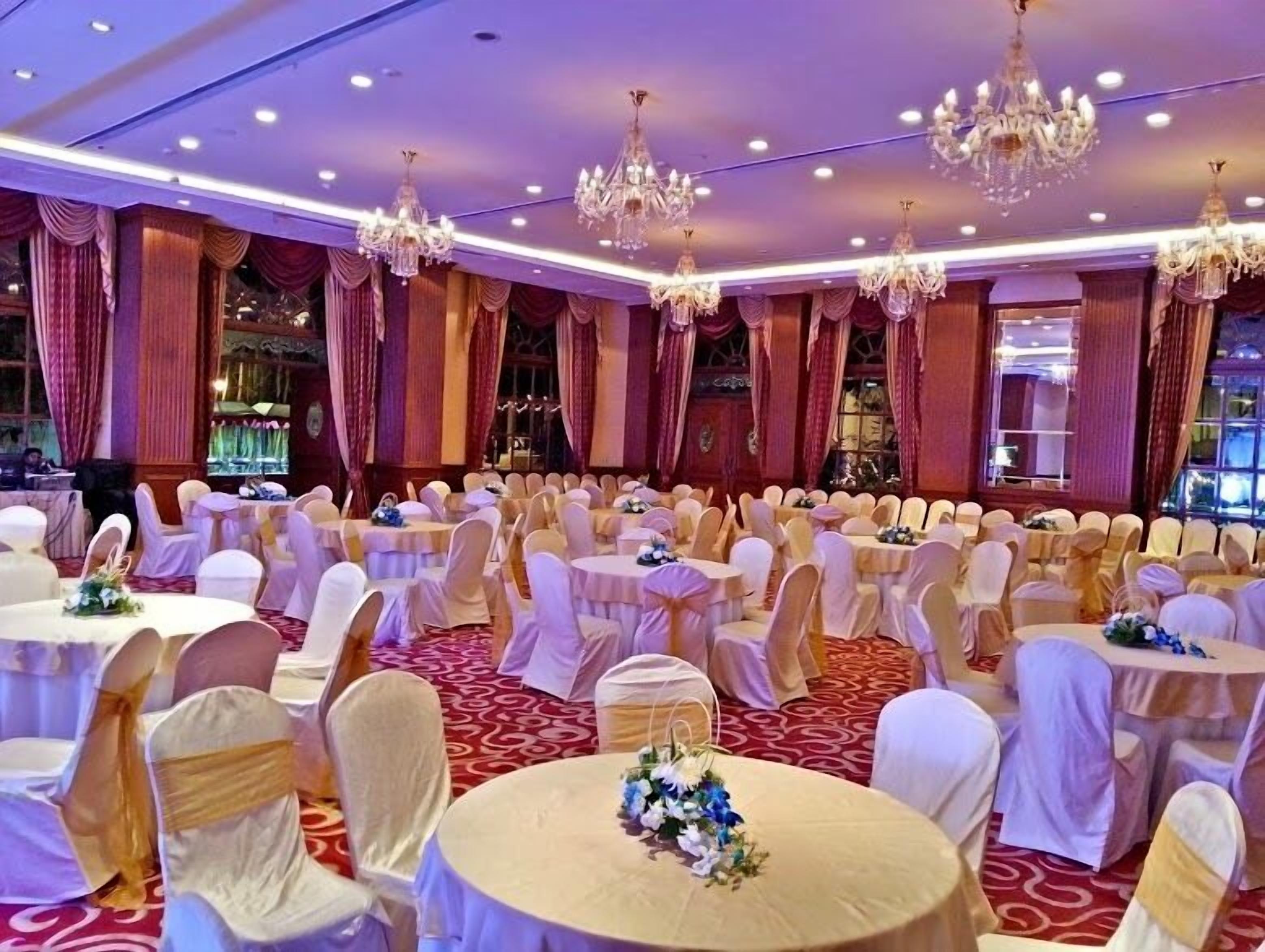 A banquet hall with round tables, white chairs, and chandeliers.