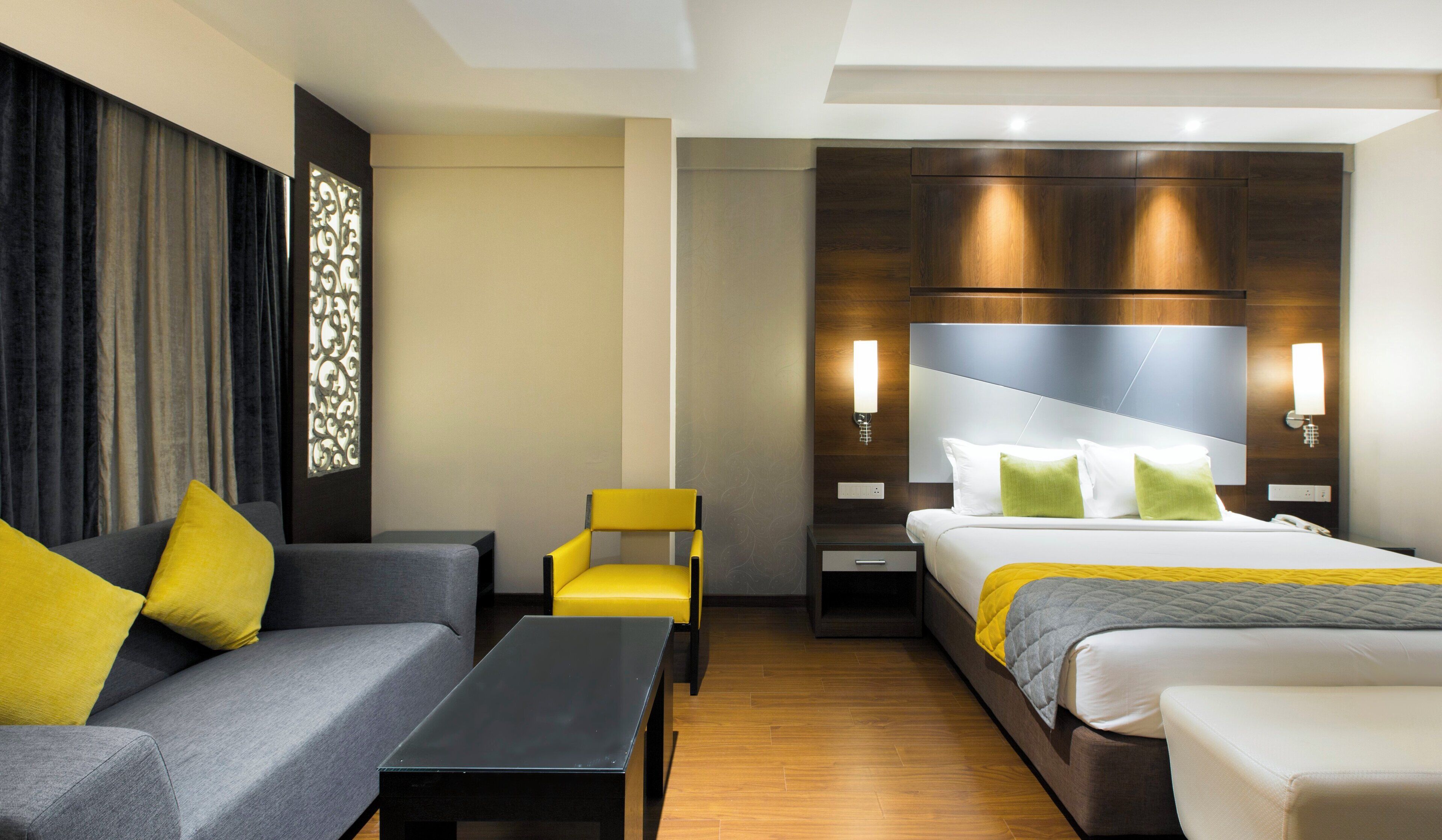 Una habitación de hotel con una cama, un sofá, una silla, una mesita de noche y una lámpara.
