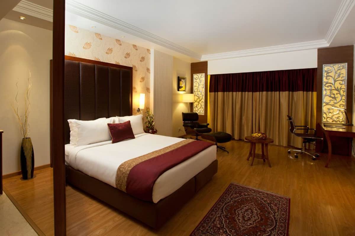 A hotel room with a large bed, a desk, a chair, a small table, and a decorative vase.