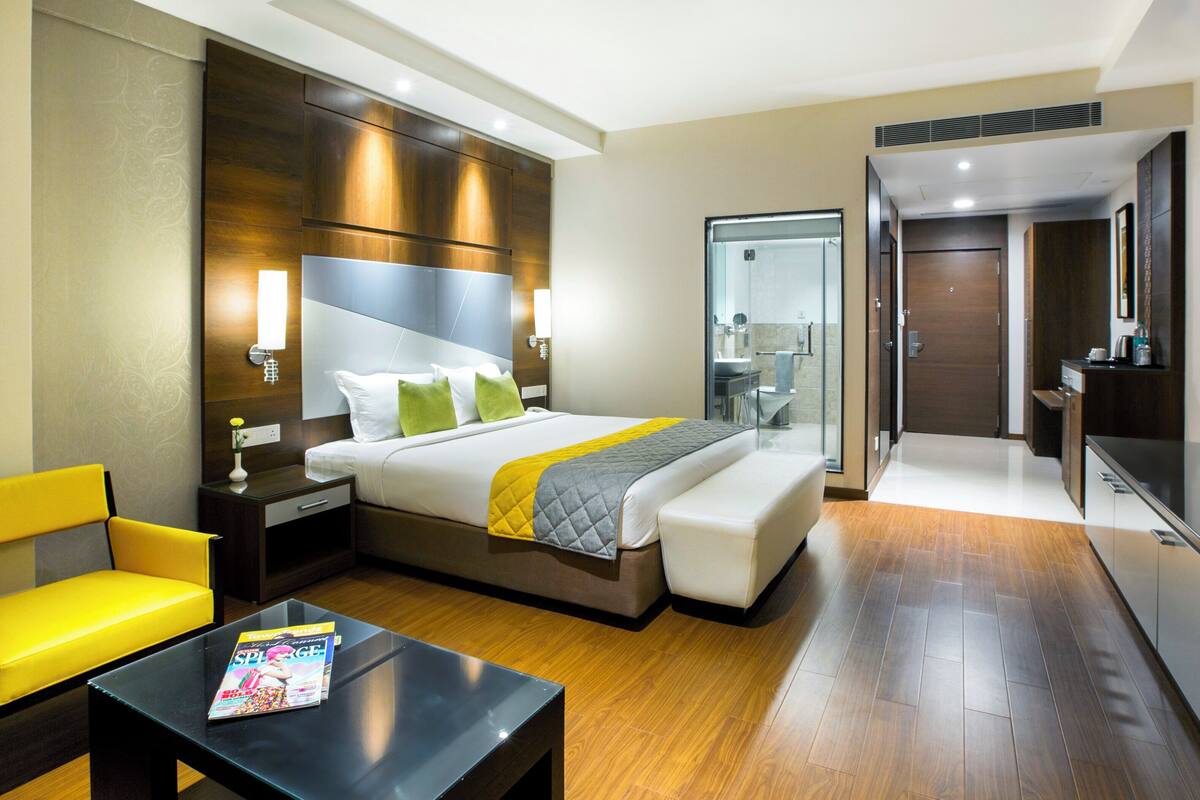 A hotel room with a bed, bedside table, chair, and a small table with a magazine.
