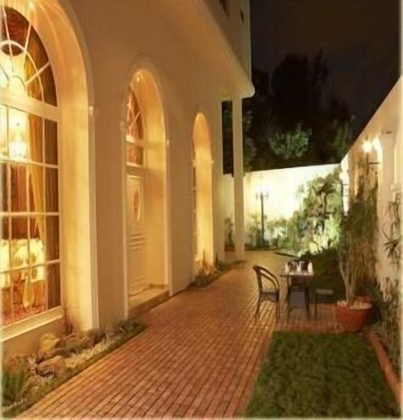 A brick pathway leading to a building with arched windows and a table with chairs outside.