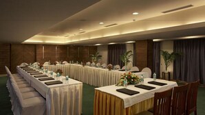 A conference room with long tables, chairs, and a stage area. - Silver Ferns (New Delhi)