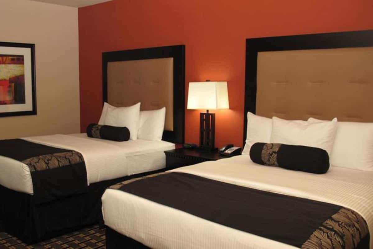 A hotel room with two beds, a nightstand with a lamp, and a framed picture on the wall.