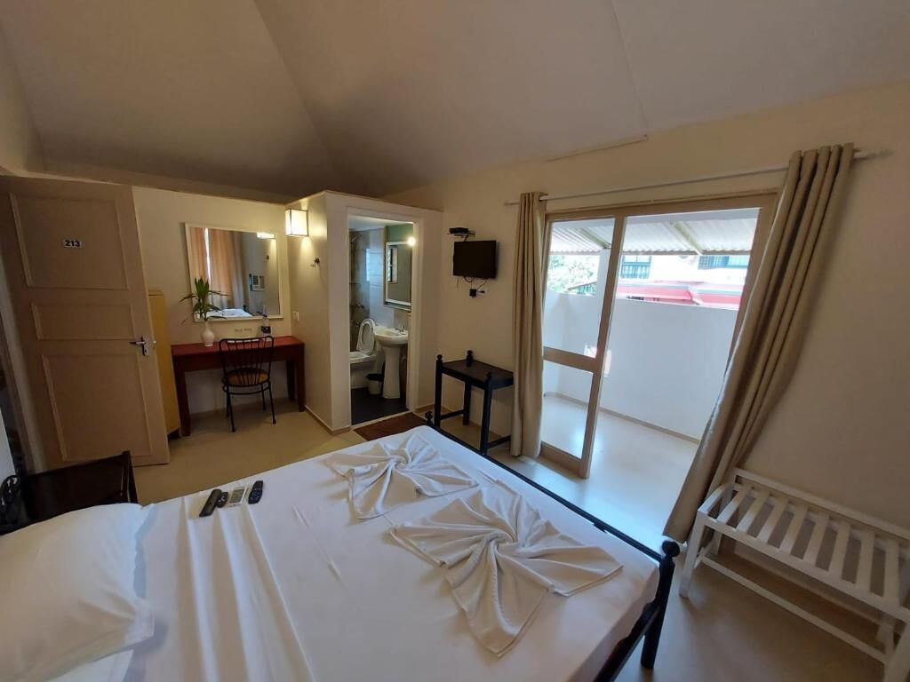 A hotel room with a bed, a desk, a chair, a television, and a sliding glass door to the outside.