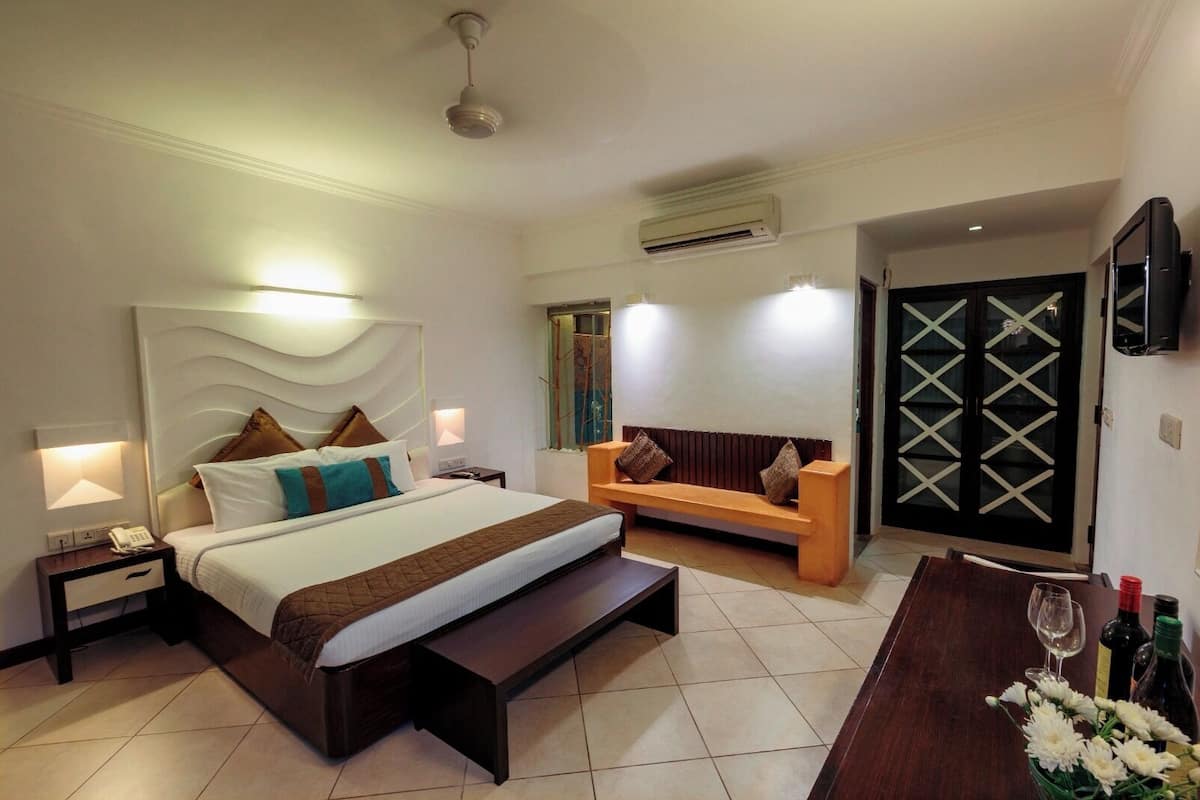 A modern hotel room with a large bed, a sofa, a desk with a chair, and a TV mounted on the wall.