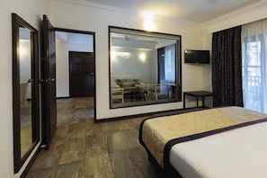 Een hotelkamer met een groot bed, een spiegel, een televisie en een zithoek die in de spiegel zichtbaar is.
