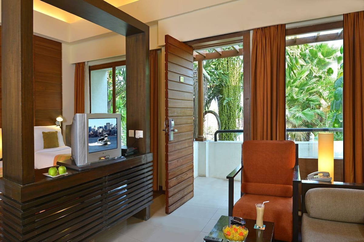 A hotel room with a bed, a television, a dining table with a remote control, and a chair.