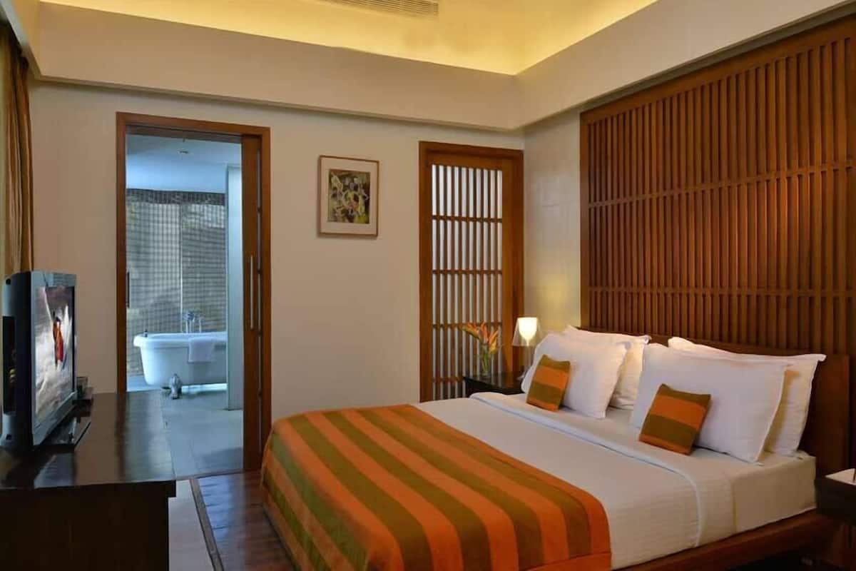 A hotel room with a bed, a television, a bathroom, and a wooden partition.