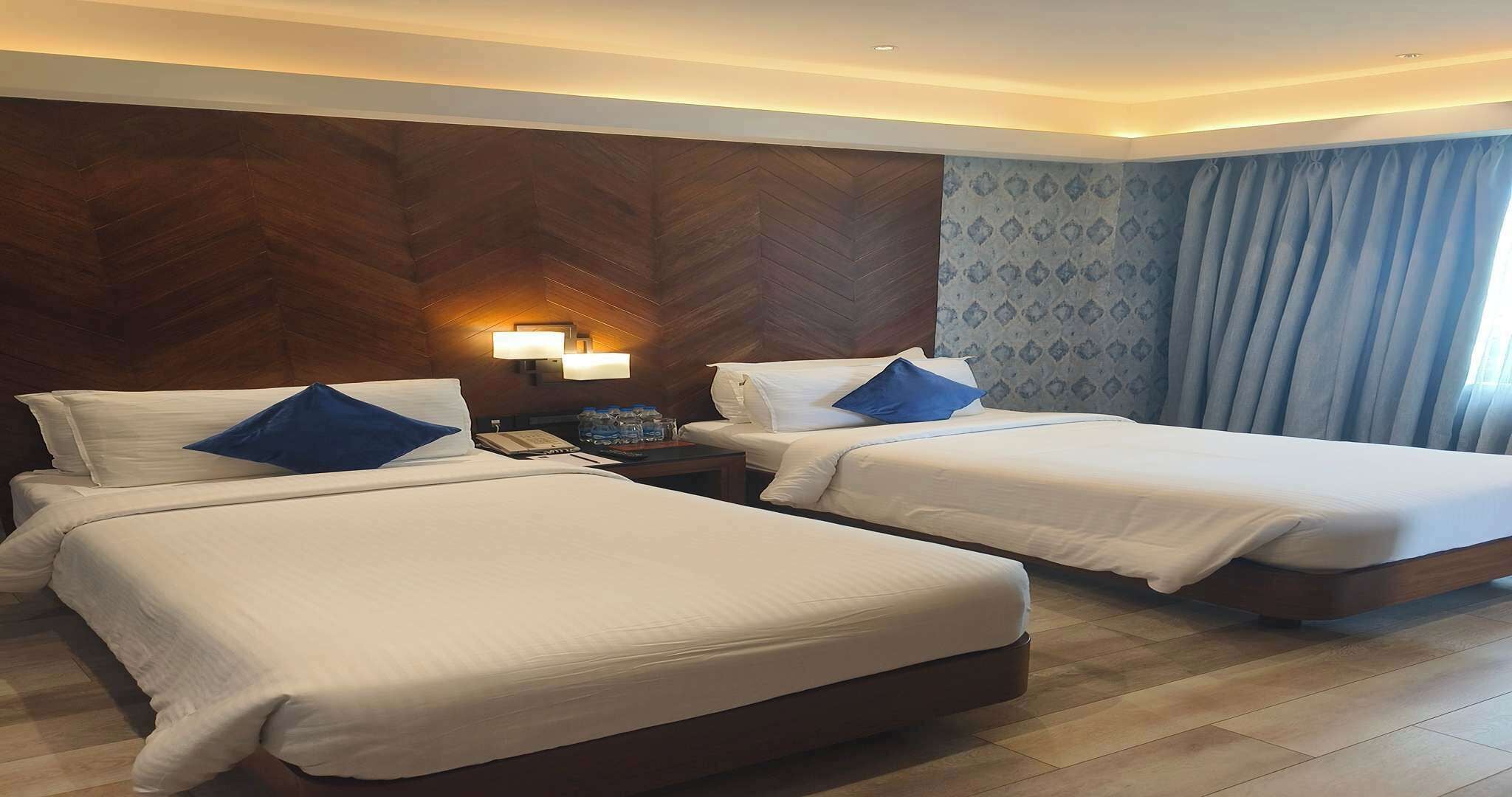 A hotel room with two beds, a nightstand, a lamp, and a patterned wall.
