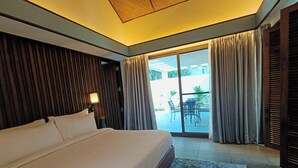 A hotel room with a large bed, a nightstand, a lamp, and a view of an outdoor patio with a table and chairs. - Golkonda Resorts & Spa (Hyderabad)