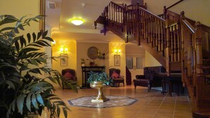 A spacious lobby with a wooden staircase, a central decorative urn, and a tiled floor. - Loch Lein Country House (Killarney)