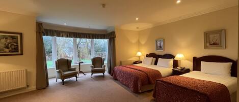 A hotel room with two beds, a sitting area with chairs, and a view of the outdoors.