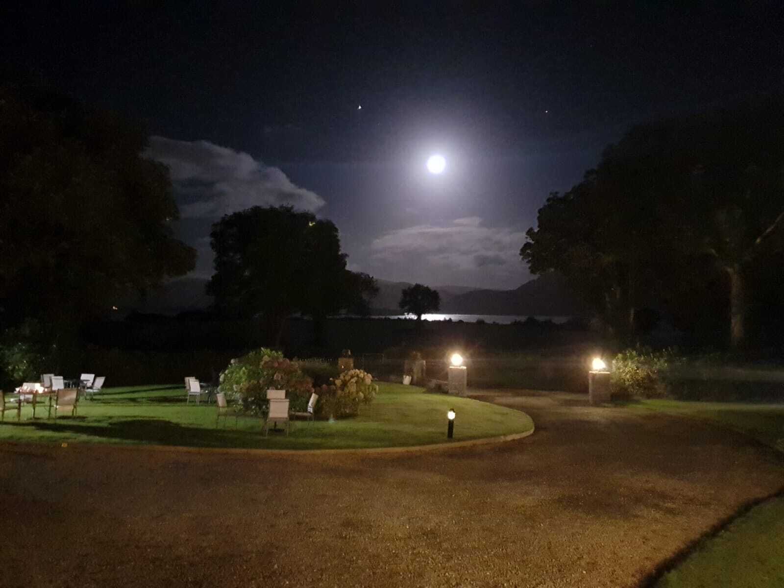 A nighttime view of a golf course with a full moon in the sky, illuminated by artificial lights.