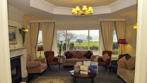 A cozy living room with a fireplace, multiple armchairs, a coffee table with books, and large windows offering a view of the outdoors. - Loch Lein Country House (Killarney)