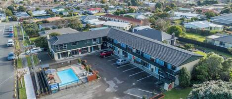 A motel with a swimming pool, parking lot, and a view of the surrounding neighborhood.