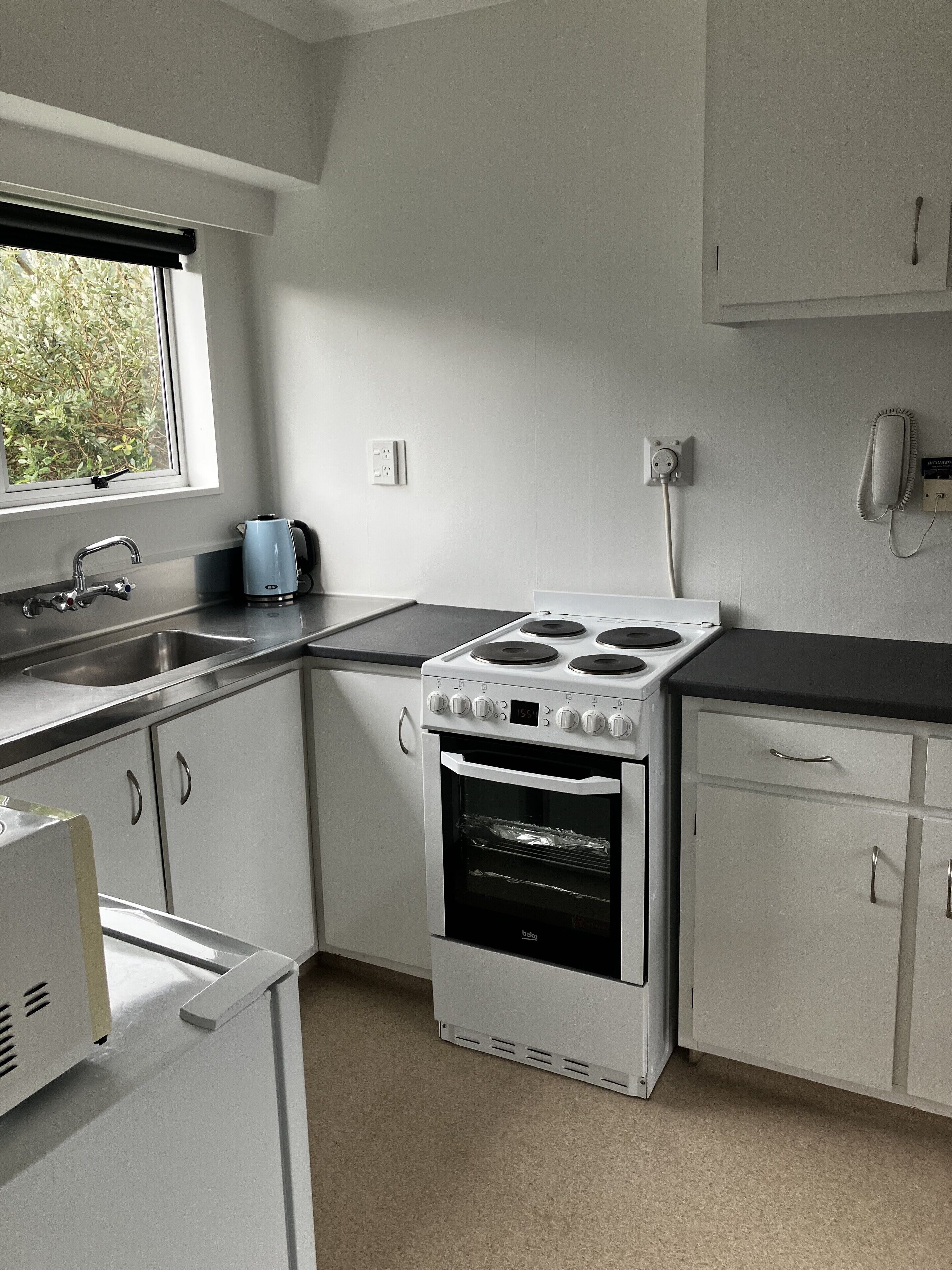 A kitchen with white cabinets, a stove, a sink, and a window with a view of greenery.