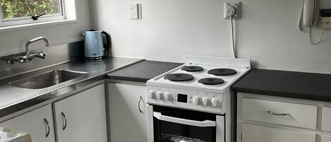 A kitchen with white cabinets, a stove, a sink, and a window with a view of greenery.
