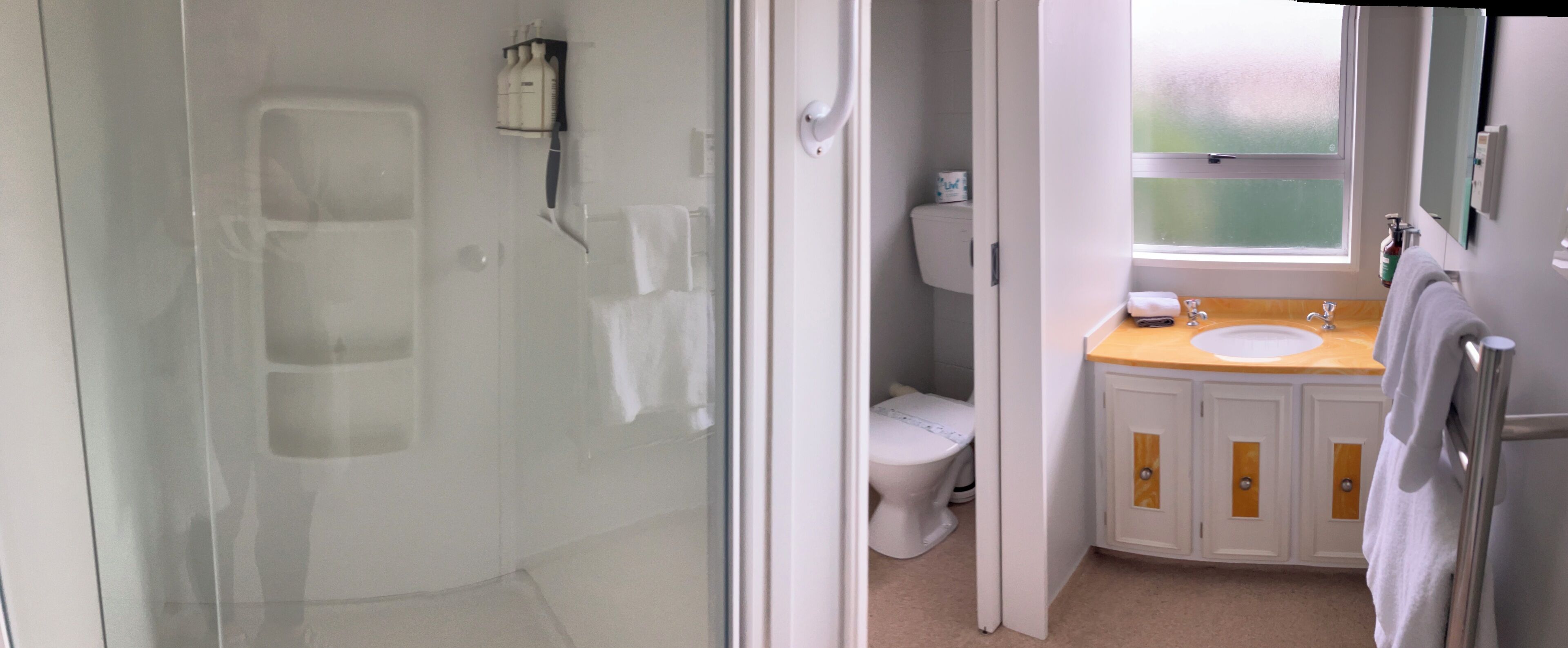 Un baño con cabina de ducha de vidrio, inodoro y lavabo con armarios de madera.