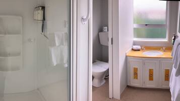 Un baño con cabina de ducha de vidrio, inodoro y lavabo con armarios de madera.