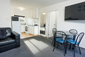 Un espacio habitable compacto con kitchenette, una zona de comedor con sillas, un sofá y un televisor de pantalla plana montado en la pared.
