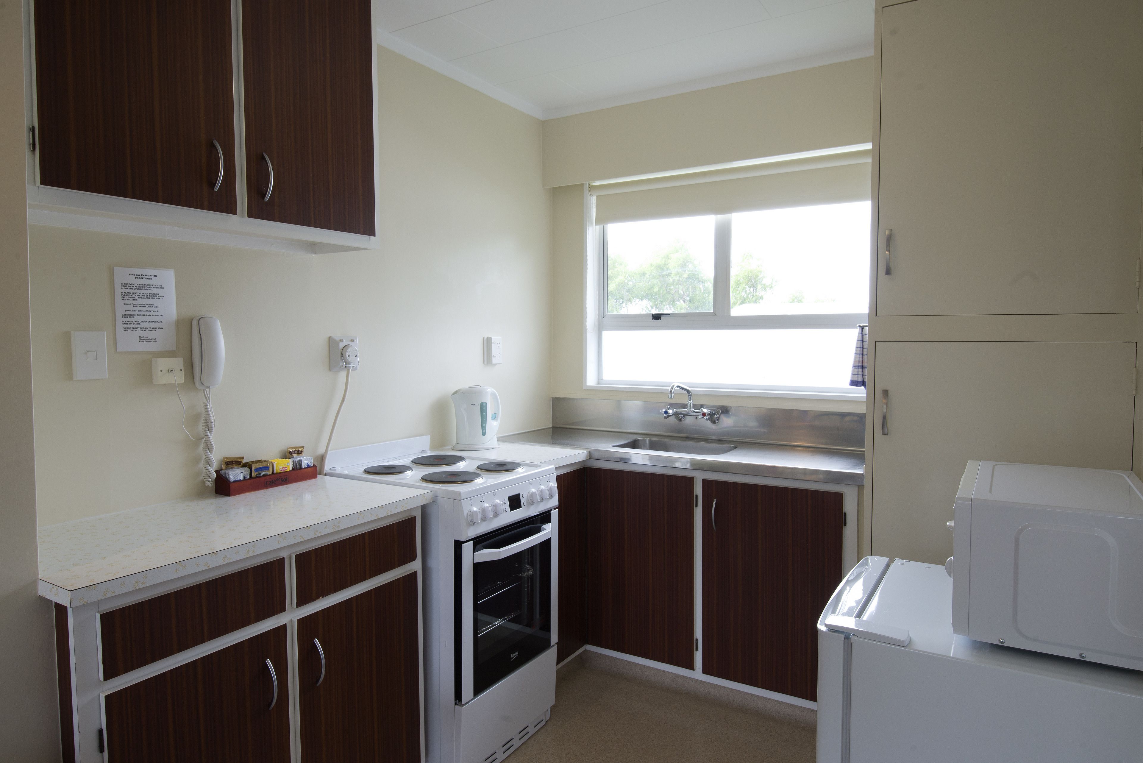 A kitchen with a stove, oven, microwave, and sink. There is a window above the sink and a cabinet above the stove.